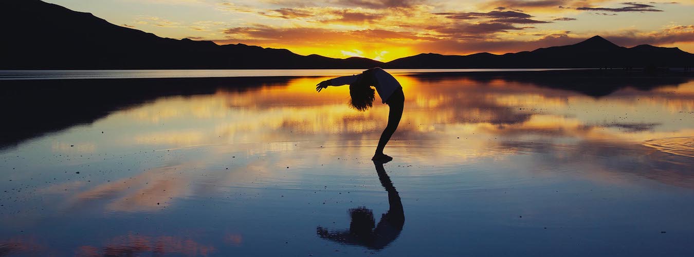 Woman doing a backbend at sea with sunset