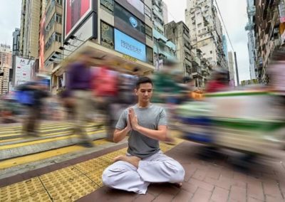 Man sitting with crossed legs on the ground of a busy street and doing Anjali Mudra