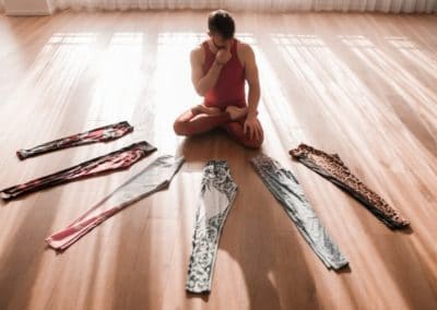 Yogi sitting on wooden floor surrounded by 6 different yoga leggings