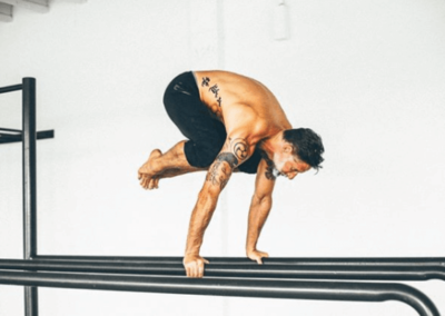 Man doing crow asana on gymnastics bars in front of a white wall