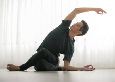 Yogi doing shoelace yoga asana while bending to his left side in a yoga studio