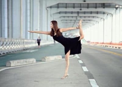 women wearing a black dress and high heels doing a yoga asana with one leg lifted with one hand