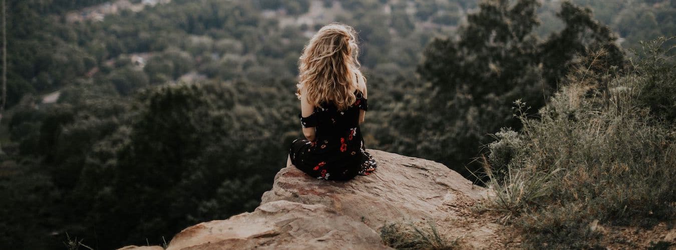 Woman sitting on a cliff in green landscape